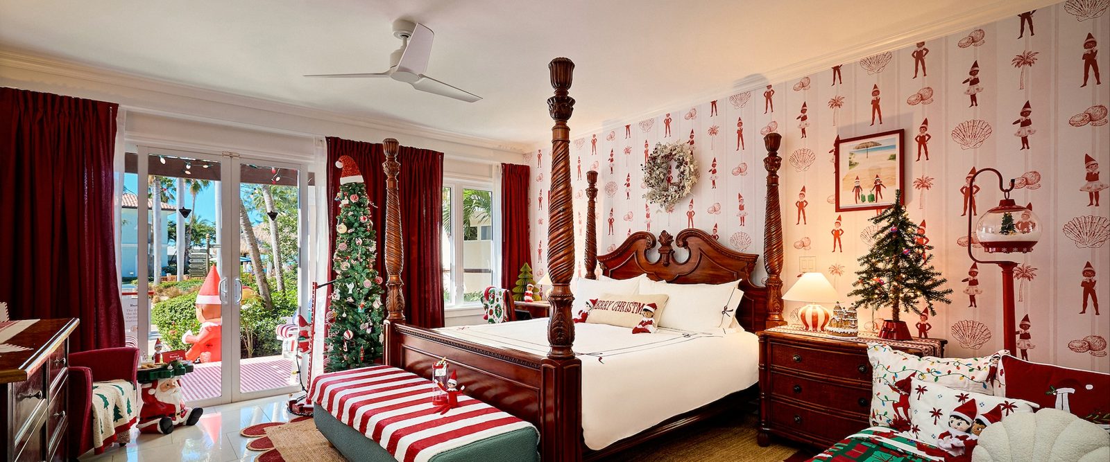 King bedroom of The Elf on the Shelf Caribbean Vacation Suite at Beaches Turks and Caicos, with a Christmas tree, Scout Elf wallpaper and a patio door to the Italian Village pool